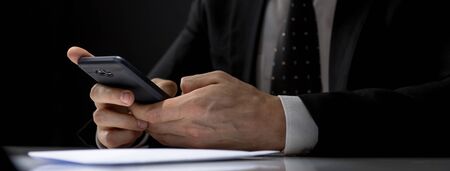 Businessman using mobile phone texting and making illegal private deal in a dark room, banner sizeの写真素材