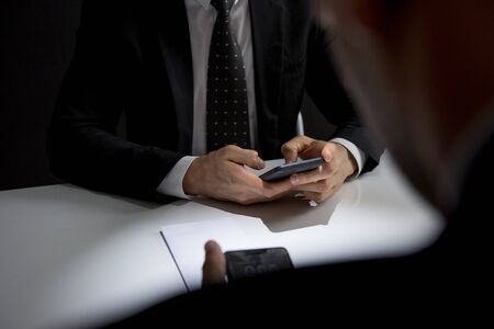 Businessmen using mobile phone texting and making illegal private deal in a dark roomの写真素材