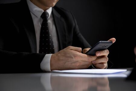Portrait of businessman using his mobile phone making illegal private deal in a dark roomの写真素材