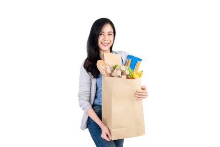 Beautiful smiling Asian woman holding paper shopping bag full of vegetables and groceries isolated on white backgroundの写真素材