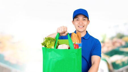 Smiling Asian man holding grocery shopping bag in supermarket offering home delivery serviceの写真素材