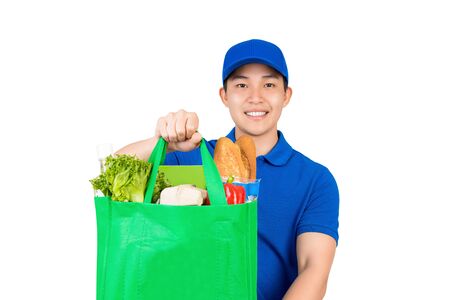 Smiling handsome Asian delivery man holding grocery shopping bag giving to customer isolated on white backgroundの写真素材