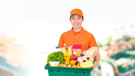 Hygienic smiling Asian man carrying supermarket grocery tray box offering home delivery serviceの写真素材