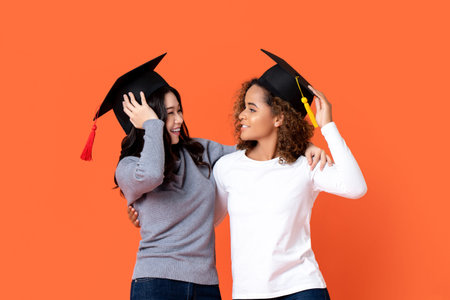 Portrait of two happy mixed-race women graduating holding there graduation caps looking at each...