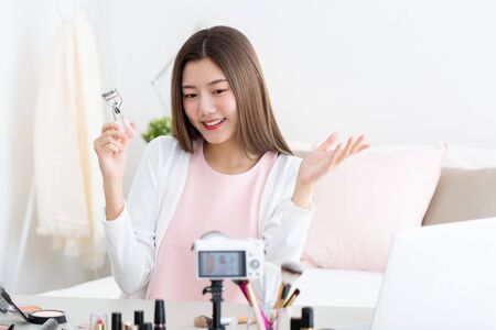 Young attractive asian woman beauty vlogger holding eyelash curler doing live streaming in front of cameraの写真素材