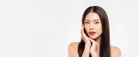 Banner beauty shot of confident Asian woman model with clear fair skin doing hands touching face pose in white isolated studio background with copy spaceの写真素材