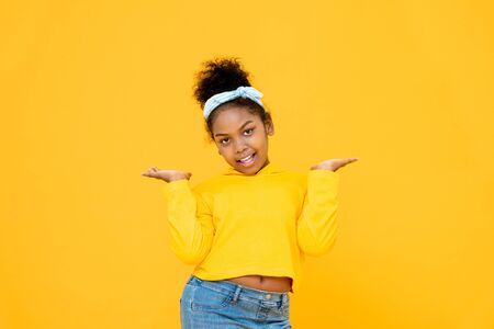 Young cute African American mixed race girl smiling and doing open palms gesture isolated on colorful yellow backgroundの写真素材