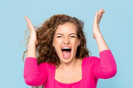 Shocked angry young Caucasian woman shouting isolated on light blue studio backgroundの写真素材