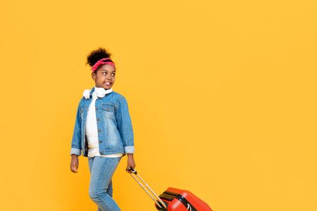 Fashionable cute African girl with luggage ready to travel isolated on yellow studio backgroundの写真素材