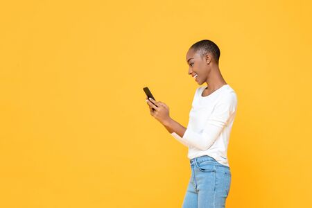 Smiling young African American woman using smartphone  isolated on yellow studio backgroundの写真素材