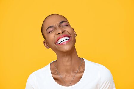 Happy optimistic African American woman laughing with eye closed isolated on colorful yellow backgroundの写真素材