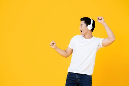 Young handsome Asian man wearing headphones listening to music and dancing on yellow backgroundの写真素材