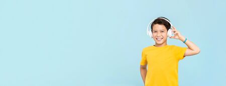 Happy smiling mixed-race boy wearing wireless headphones listening to music isolated on light blue banner background with copy spaceの写真素材