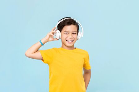 Happy smiling mixed-race boy wearing wireless headphones listening to music isolated on light blue backgroundの写真素材