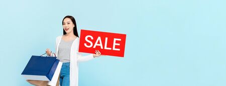 Surprised Asian woman holding red sale sign isolated on light blue banner background with copy spaceの写真素材