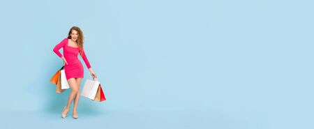 Smiling Caucasian woman with colorful shopping bags standing on light blue isolated banner background with copy spaceの写真素材