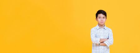 Sulky bored boy pouting mouth and thinking with arm crossed gesture isolated yellow banner backgroundの写真素材