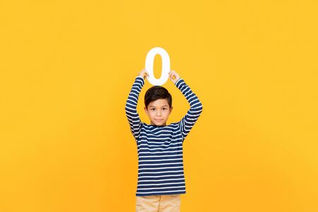 10 year-old cute little boy holding number zero overhead on yellow backgroundの写真素材