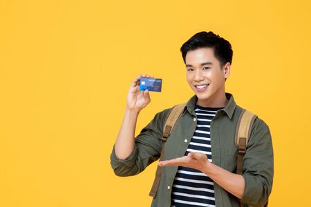 Young smiling Asian tourist man holding credit card ready to travel isolated on yellow backgroundの写真素材