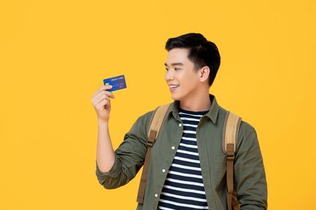 Young Asian tourist man holding credit card ready to travel isolated on yellow backgroundの写真素材
