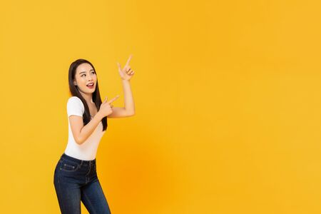 Portrait of smiling young beautiful Asian woman pointing up with her two fingers in blank space beside in yellow isolated studio backgroundの写真素材
