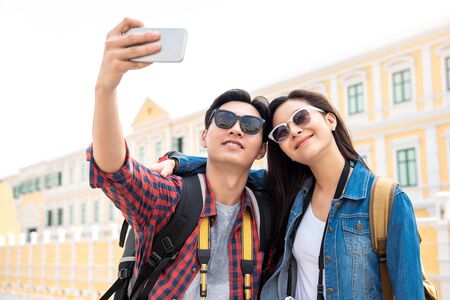 Portrait of young happy Asian tourist couple in casual attire taking a selfie while traveling in Bangkok Thailandの写真素材