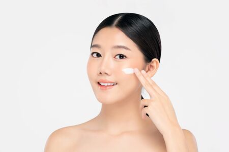 Young beautiful Asian woman with fresh clean appearance applying cream to face isolated on white background for beauty and skin care conceptsの写真素材