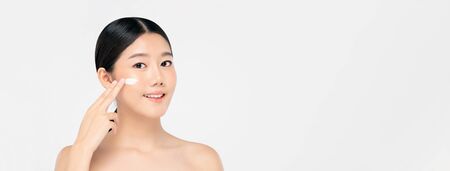 Young beautiful Asian woman with fresh clean appearance applying cream to face isolated on white background for beauty and skin care conceptsの写真素材