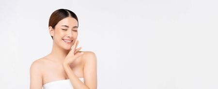 Youthful bright skin smiling pretty Asian woman with hand touching face and eyes closing on white banner background for beauty conceptsの写真素材