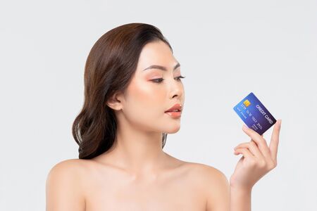 Youthful skin Asian woman showing credit card isolated on white background for beauty treatment promotion and payment conceptsの写真素材