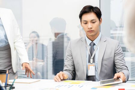 Asian Vietnamese businessman seriously reading project documents at the meeting in city officeの写真素材