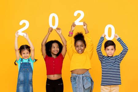 Cute mixed race kids smiling and holding 2020 numbers for new year concept isolated on yellow  backgroundの写真素材