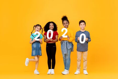 Cute mixed race kids smiling and holding 2020 numbers for new year concept isolated on yellow backgroundの写真素材