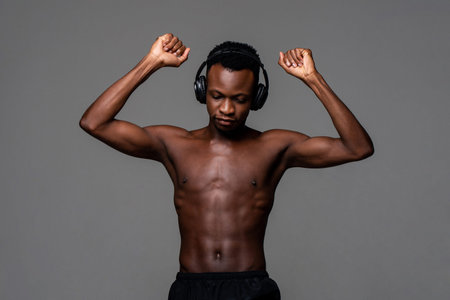 Shirtless African man with headphone listening to music while standing on gray isolated background...