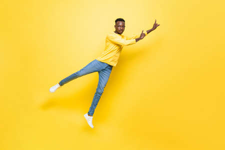 Full body of African man in casual wear levitating and pointing hands up on isolated yellow background in studioの写真素材