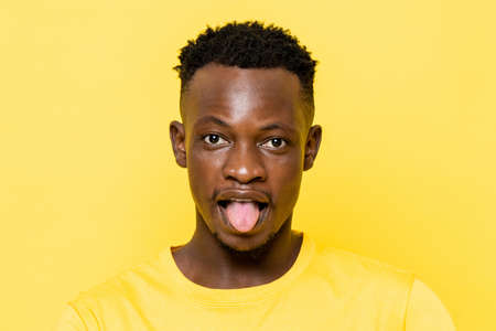 African man sticking his tongue out on yellow color background in light studioの写真素材