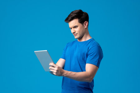 Young handsome Caucasian man holding tablet computer in isolated light blue studio backgroundの写真素材