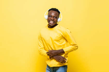 Young cheerful African man wearing headphones listening to music and dancing in isolated yellow color studio backgroundの写真素材