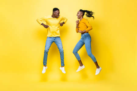 Joyful smiling young African American couple jumping in yellow isolated studio backgroundの写真素材