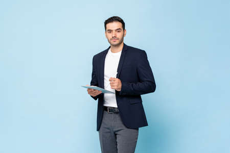 Smart handsome Caucasian man in semi formal business suit holding tablet computer with pen in light blue color  isolated studio backgroundの写真素材