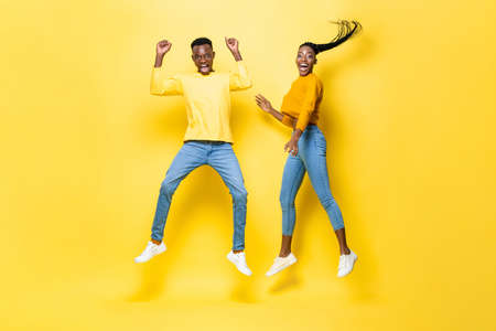 Surprised excited African couple jumping in studio isolated yellow color backgroundの写真素材