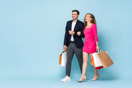 Happy Caucasian couple with shopping bags walking in studio light blue color isolated background with copy spaceの写真素材