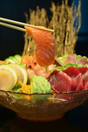 sliced raw salmon with chopsticks holding it on sashimi setの写真素材