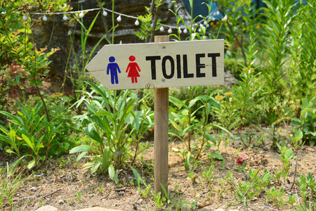 Wooden sign pointing way in garden to restrooms or toiletsの写真素材