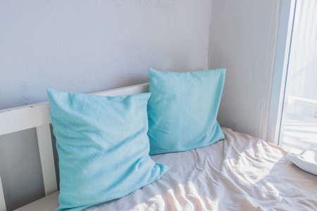 Picture two blue pillows resting on a white wooden sofa in a living room with lighted windows.の写真素材