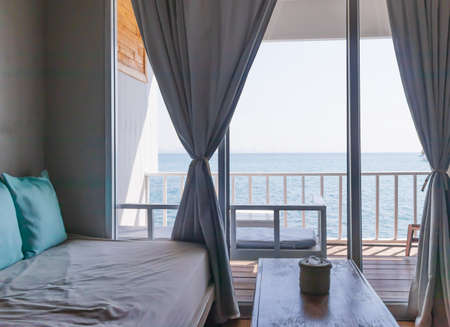 The interior of the hall with a balcony next to the sea, with a sofa and white curtains by the window and blue pillows.の写真素材