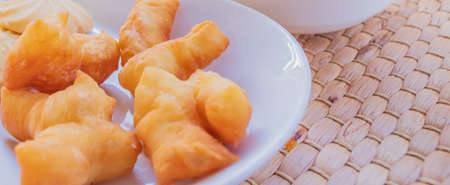 Close-up shot of breakfast with deep-fried dough stick placed on a white plate against a wicker basket background.の写真素材