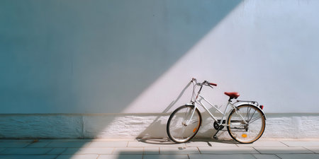 Bicycle parked beside white wall with sunlight casting shadow on tiled floor creating calm atmosphereの素材