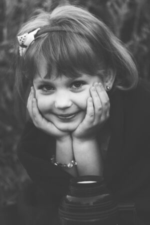 smiling girl looks clasped hands under chinの写真素材