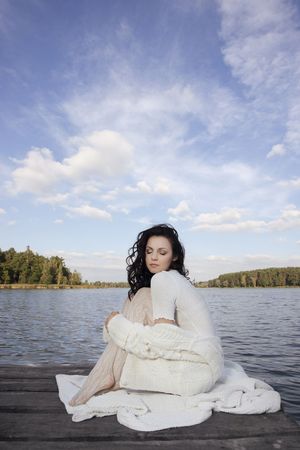Fashion shot of beautiful woman wearing white sitting alone on the pier の写真素材
